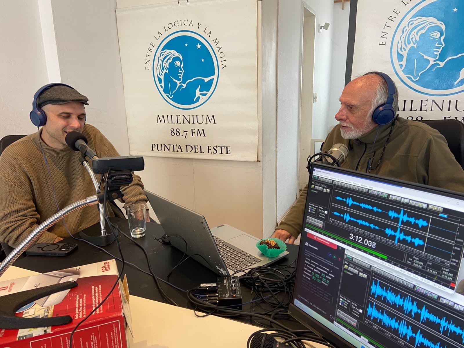 Una entrevista en el estudio de Milenium FM: dos personas frente a los micrófonos, con la consola y el editor de audio abiertos.